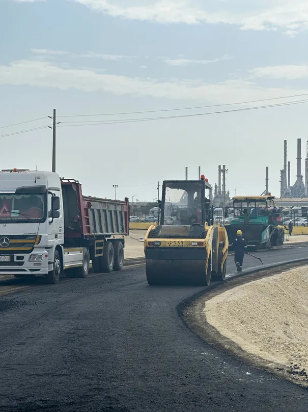 Roller compacting fresh asphalt beside a refinery