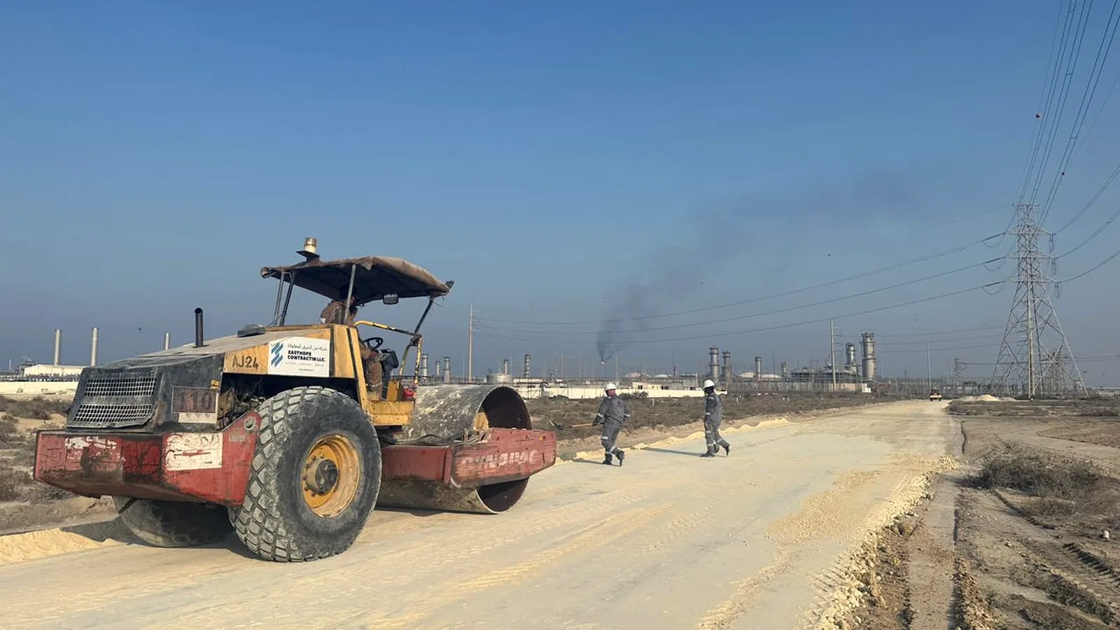 Roller compacting a road beside a gas plant