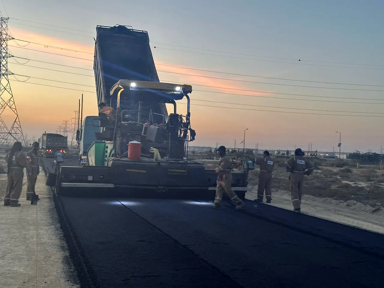 Asphalt paver and crew laying a road at dusk